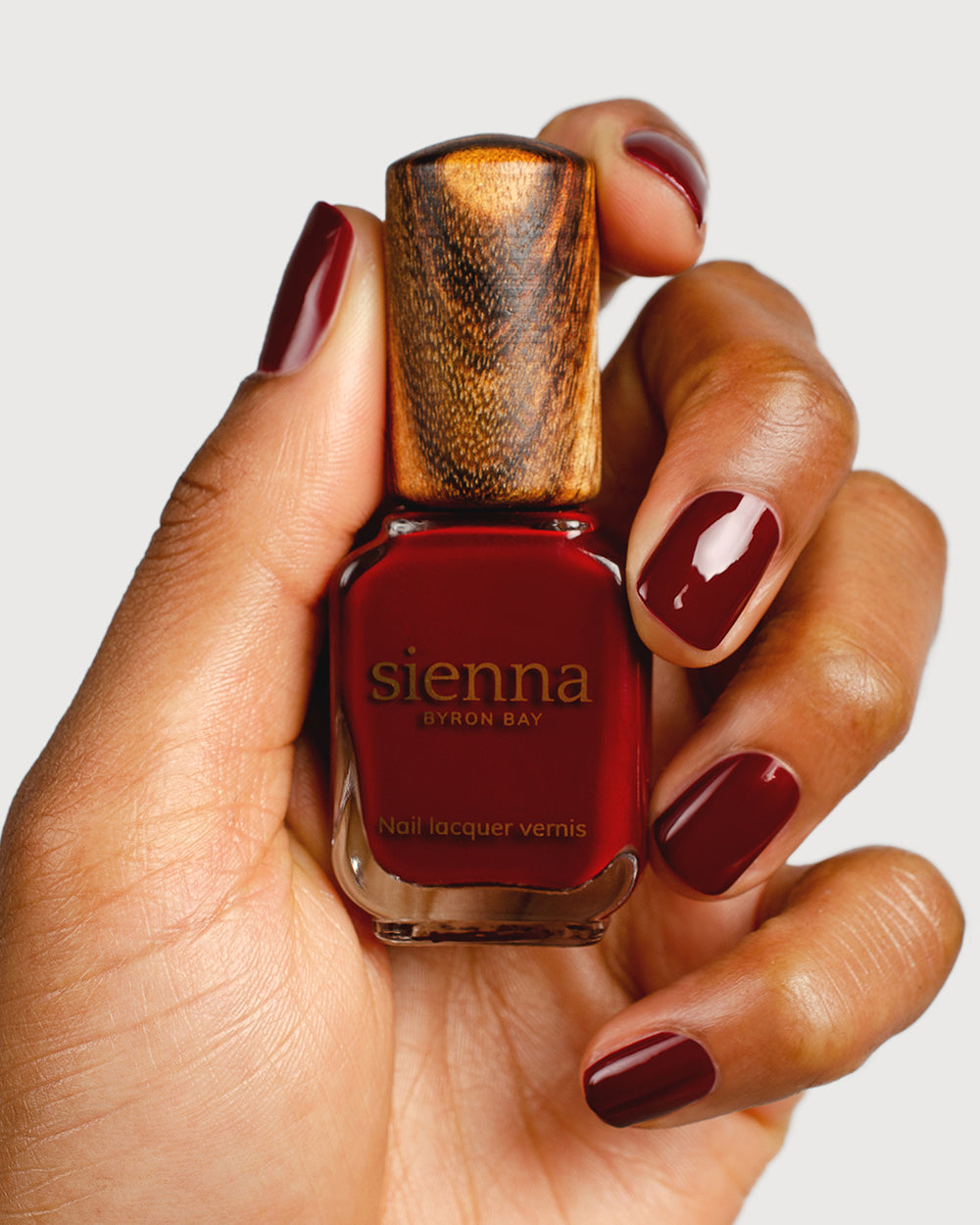 Organic mid-tone red nail polish hand swatch on Medium skin tone up-close holding sienna bottle